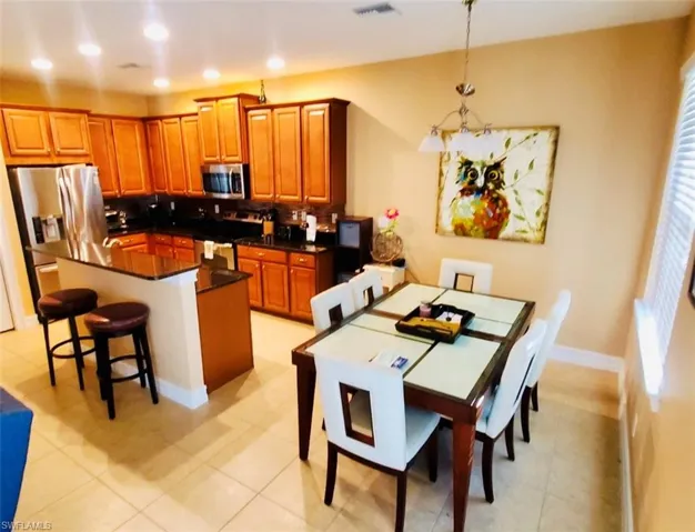 Kitchen with a breakfast bar area, brown cabinets, stainless steel appliances, dark stone counters, and recessed lighting