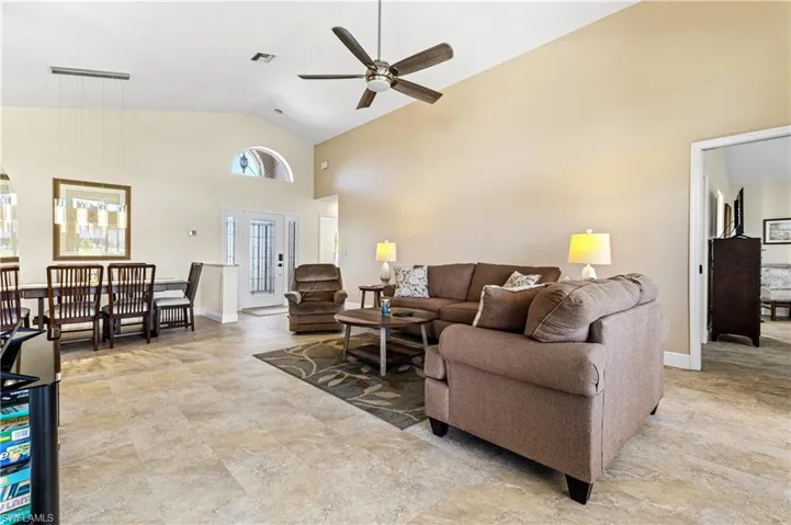 Living area with visible vents, high vaulted ceiling, ceiling fan, and baseboards