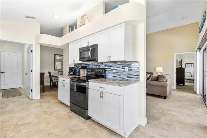 Kitchen with visible vents, white cabinets, black electric range, decorative backsplash, and stainless steel microwave
