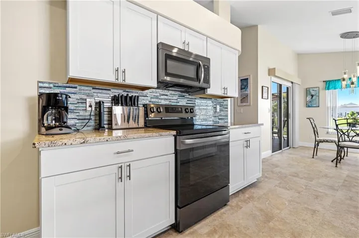 Kitchen with tasteful backsplash, baseboards, appliances with stainless steel finishes, white cabinetry, and pendant lighting