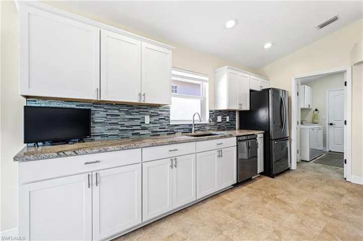 Kitchen featuring a sink, visible vents, white cabinets, black appliances, and washer and clothes dryer