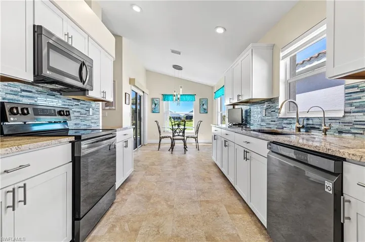 Kitchen with lofted ceiling, visible vents, appliances with stainless steel finishes, white cabinets, and a sink