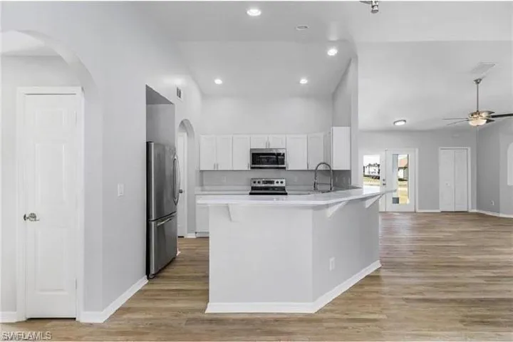 Kitchen featuring appliances with stainless steel finishes, a peninsula, white cabinets, a ceiling fan, and arched walkways