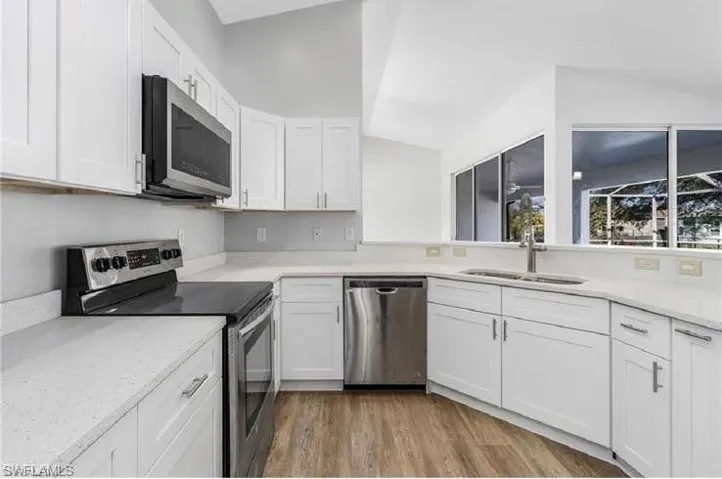 Kitchen featuring appliances with stainless steel finishes, white cabinets, wood finished floors, and lofted ceiling