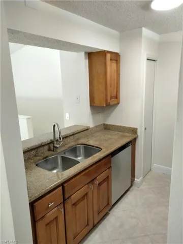 Kitchen with stainless steel dishwasher, light stone countertops, light tile patterned floors, sink, and a textured ceiling