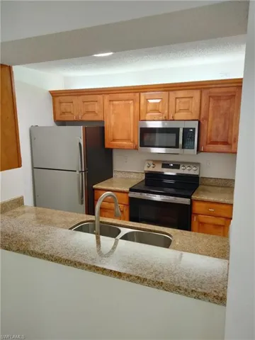 Kitchen featuring sink, stainless steel appliances, a textured ceiling, and light stone countertops