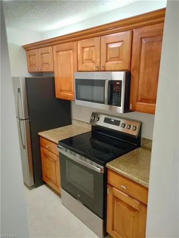 Kitchen featuring light tile patterned floors, stainless steel appliances, a textured ceiling, and light stone countertops