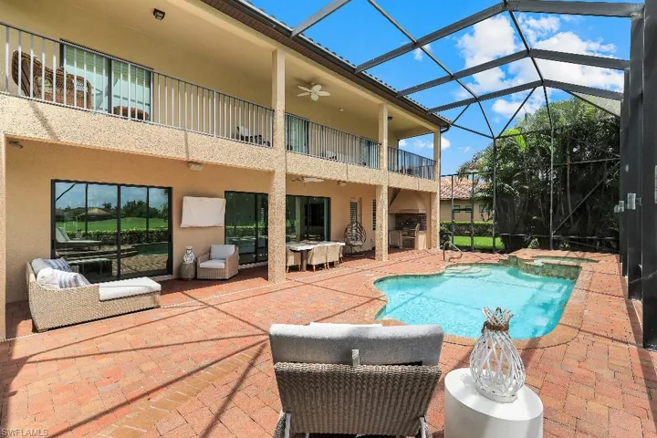 Screened-in outdoor living space featuring a freeform pool, integrated spa, and brick paver decking