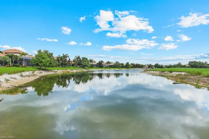 Waterfront property featuring a tranquil lake, lush green landscaping, and mature palm trees