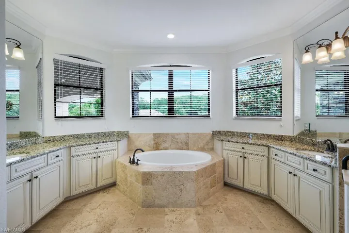 Bathroom featuring a built-in soaking tub, dual vanity areas with granite countertops, light-toned cabinetry, and tile flooring