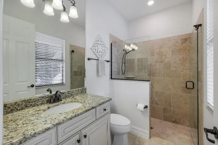 Bathroom featuring a granite countertop vanity with integrated sink, white cabinetry, and bronzed hardware