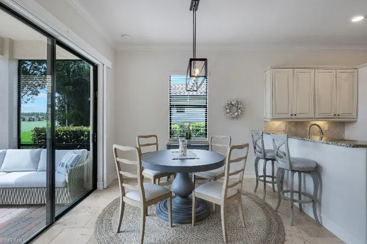 Sliding glass doors opening to a screened patio, stone tile flooring, a kitchen bar with a granite countertop, and light-toned cabinetry with dark hardware