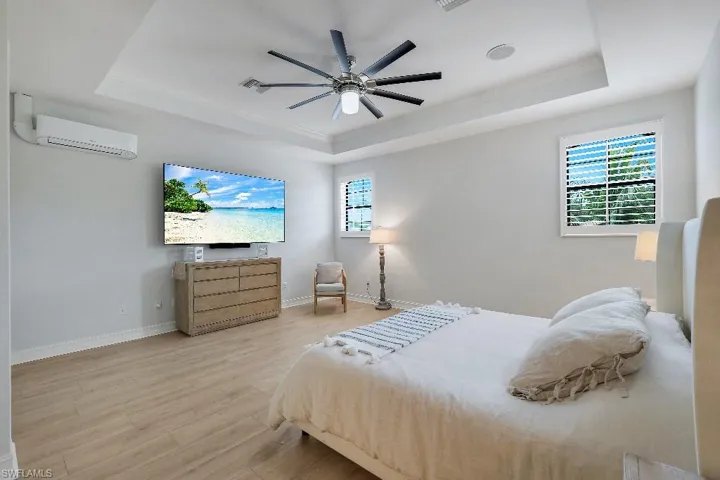 Spacious room featuring wood-finish flooring, a tray ceiling, and a ceiling fan with integrated lighting