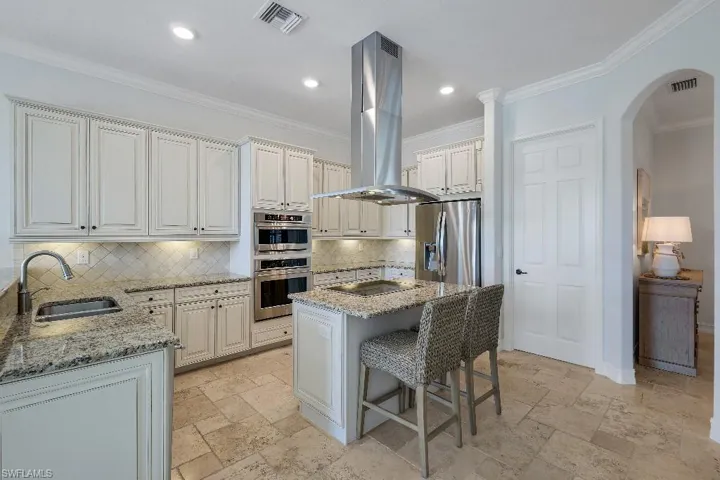 Kitchen featuring light-toned cabinetry, stainless steel appliances, an island with cooktop and range hood, stone countertops, and tile flooring