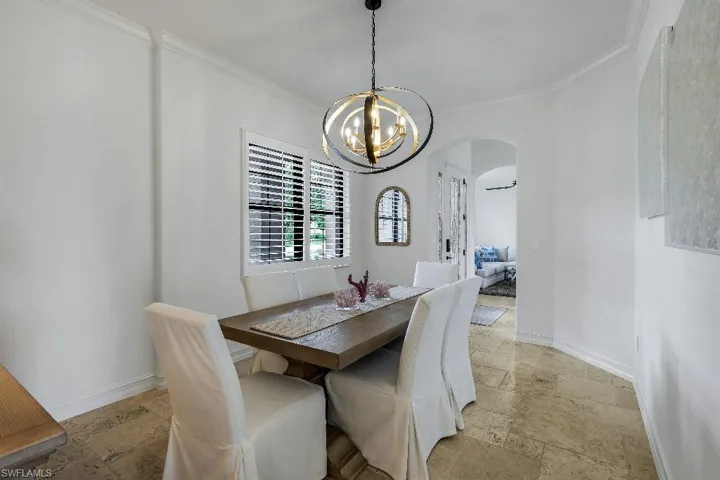 Dining space featuring a spherical chandelier, plantation shutters, an arched doorway, crown molding, and stone tile flooring