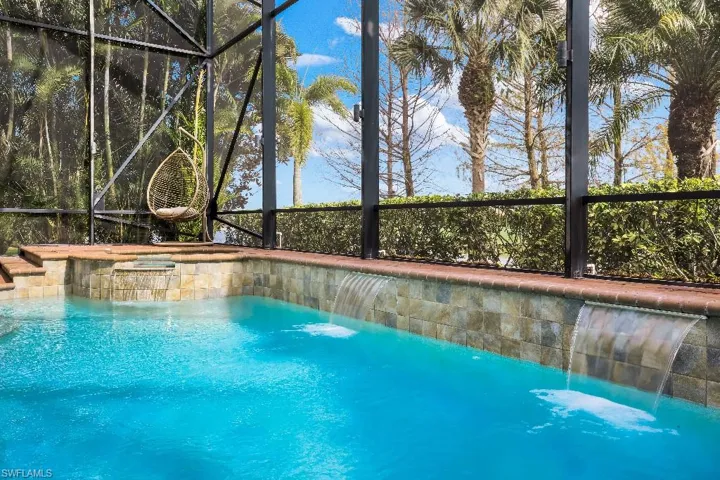 Screened swimming pool featuring multiple waterfall features, stone-tiled spa, and surrounding tropical foliage