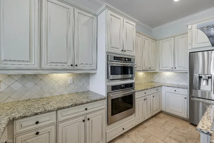 Kitchen featuring white cabinetry with dark hardware, granite countertops, a diagonal tile backsplash, stainless steel double oven, and a stainless steel refrigerator