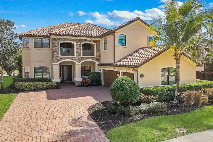 Stucco and stone exterior featuring an arched entry, tile roof, and a paver driveway