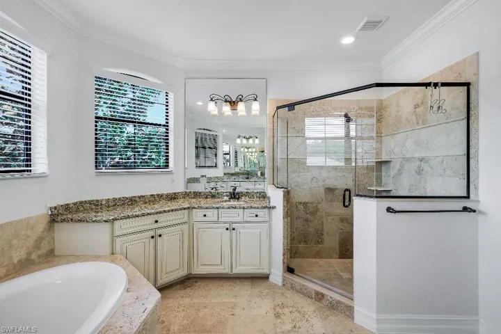 Spacious bathroom featuring a glass-enclosed shower with tile surround, a built-in soaking tub, a double vanity with granite countertop, and light-toned tile flooring