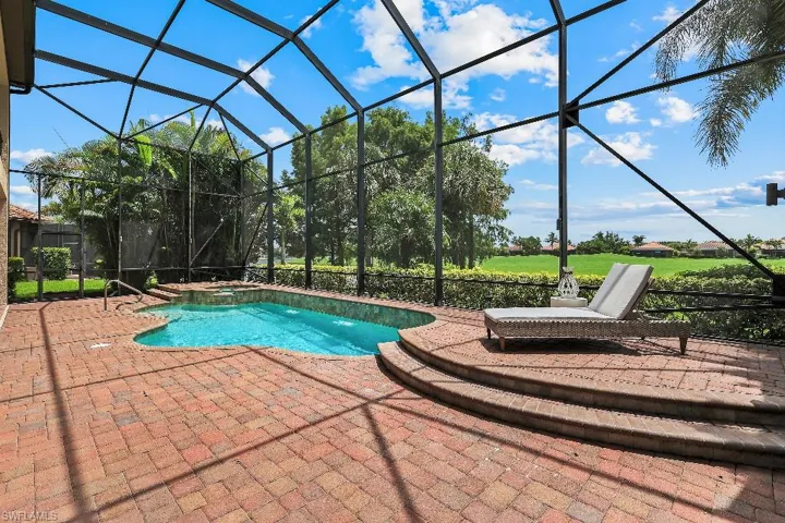 Screened-in outdoor living space featuring a free-form pool with water feature, brick paver patio, and two-tiered patio area