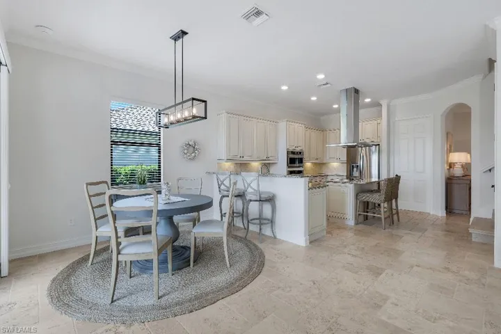 Open-concept kitchen and dining area featuring light-toned cabinetry, light-toned flooring, stainless steel appliances, and a kitchen island with seating