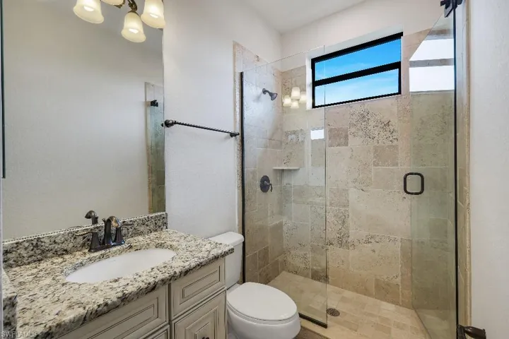 Bathroom featuring a glass-enclosed shower with stone-finish tile, a built-in shower shelf, a vanity with a granite-finish countertop, and a single basin sink