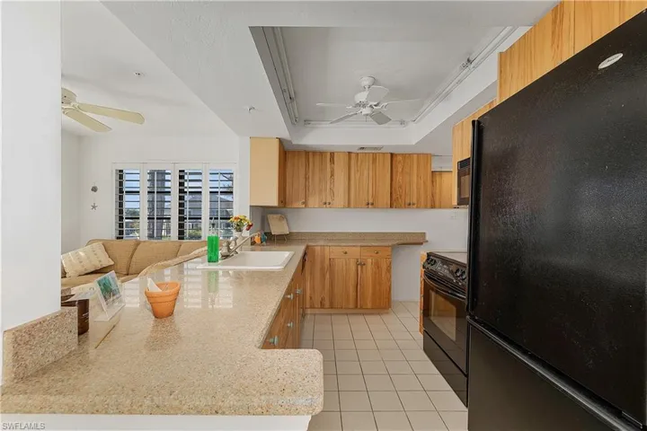 Kitchen with ceiling fan, black appliances, a peninsula, light tile patterned flooring, and a tray ceiling