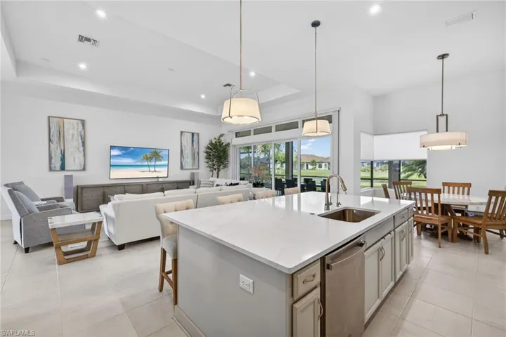 Kitchen with pendant lighting, light stone counters, a kitchen breakfast bar, a kitchen island with sink, and dishwasher
