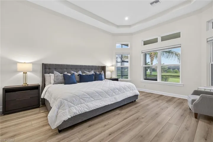Bedroom with light wood-type flooring, a towering ceiling, a raised ceiling, and recessed lighting