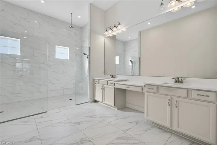 Bathroom with a marble finish shower, light marble finish flooring, and double vanity