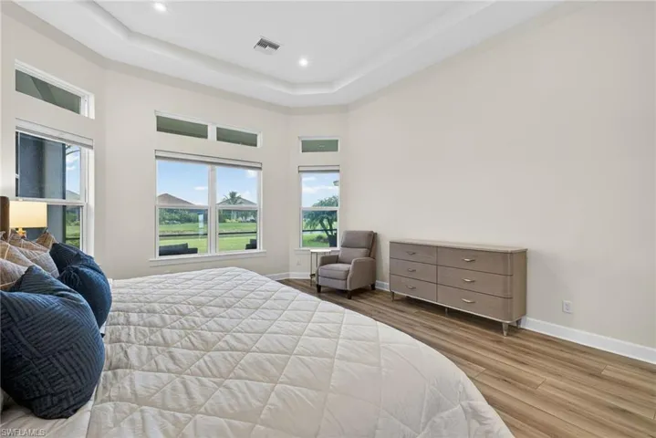 Bedroom with light wood-style flooring, a tray ceiling, a towering ceiling, and recessed lighting
