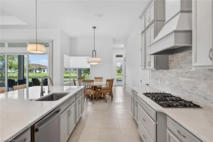 Kitchen featuring light stone countertops, decorative light fixtures, backsplash, appliances with stainless steel finishes, and light tile patterned flooring