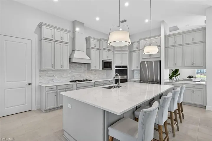 Kitchen featuring gray cabinets, a kitchen breakfast bar, stainless steel appliances, an island with sink, and decorative light fixtures