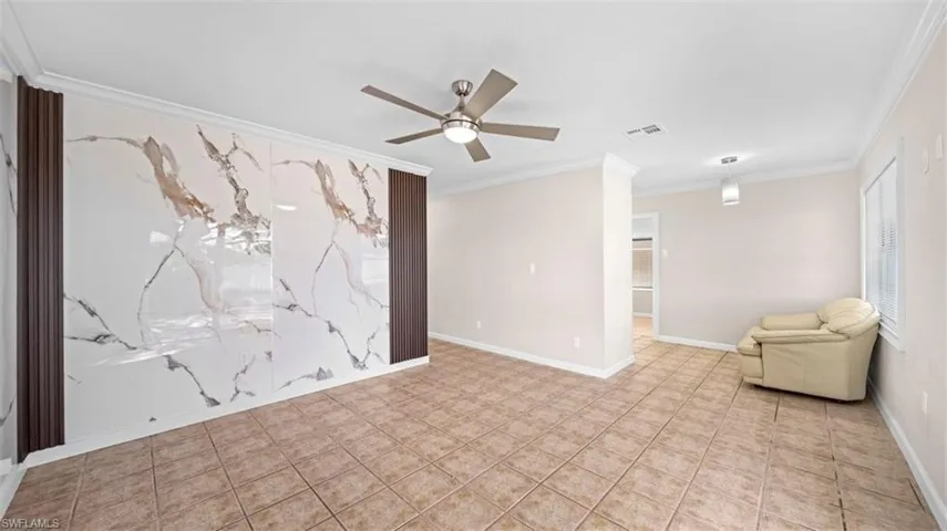 Tiled spare room featuring a ceiling fan, crown molding, and an accent wall