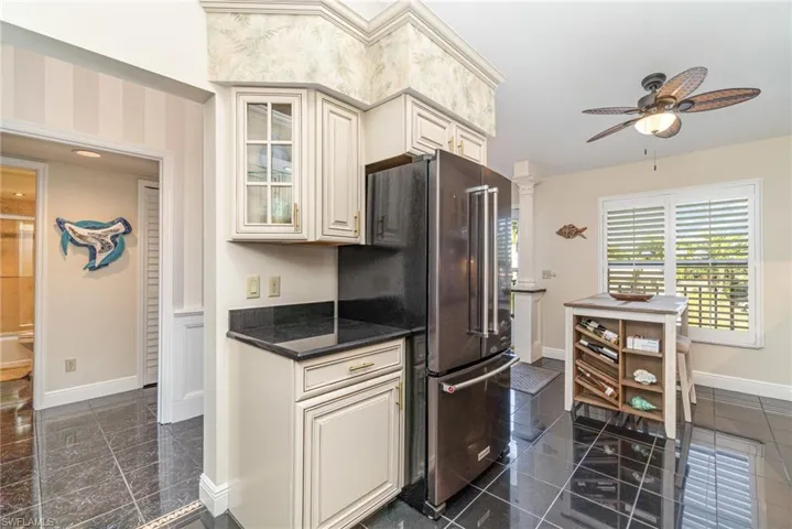 Kitchen with freestanding refrigerator, cream cabinetry, glass insert cabinets, and granite tiled floors