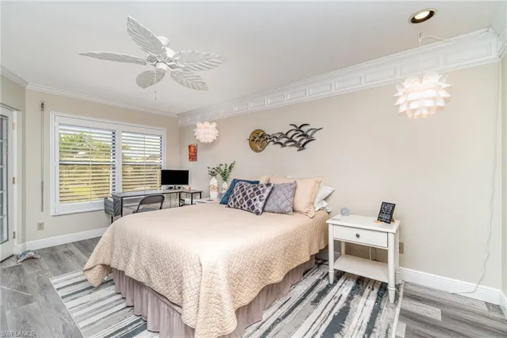 Bedroom with crown molding, a ceiling fan, an office area, and light wood-style floors