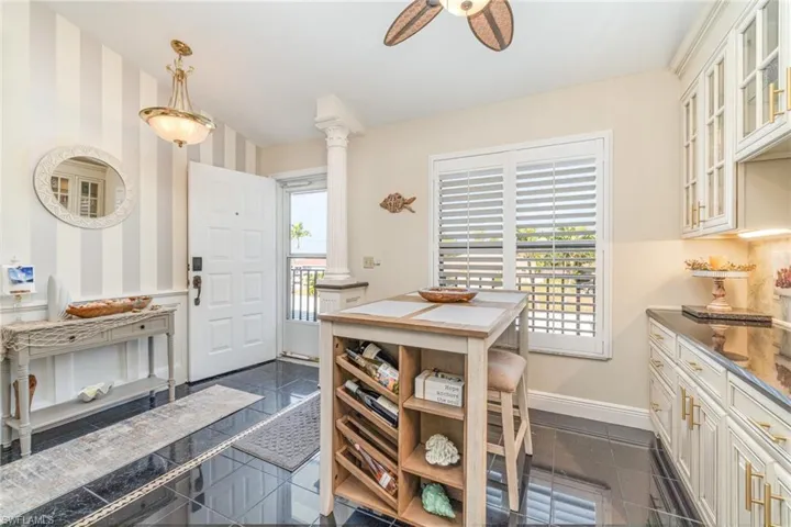Kitchen featuring glass insert cabinets, granite tiled floors, wallpapered walls, a wainscoted wall, and decorative light fixtures