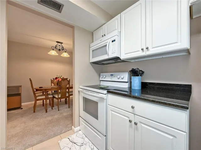Kitchen with  a chandelier, white appliances, white cabinetry, and light colored carpet