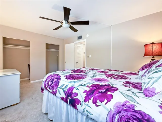 Bedroom with light colored carpet, baseboards, multiple closets, ceiling fan, and visible vents