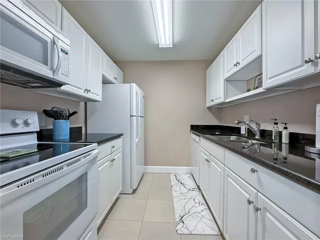 Kitchen featuring white cabinetry, white appliances, light tile patterned floors, dark stone countertops, and a sink