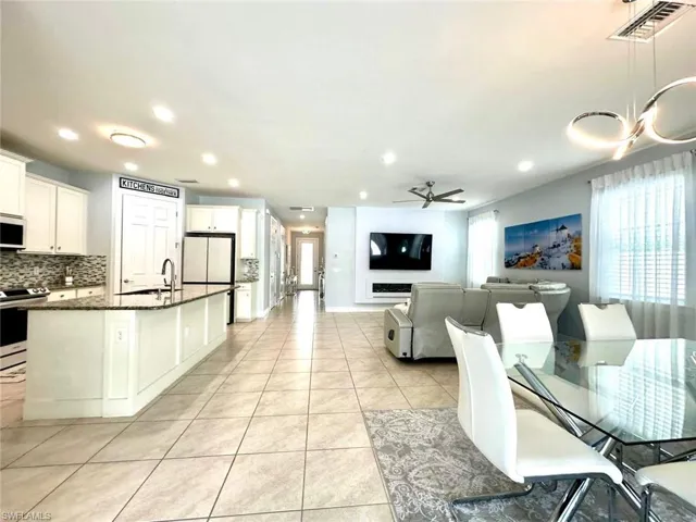 Kitchen featuring light tile patterned flooring, white appliances, backsplash, white cabinets, and a center island with sink