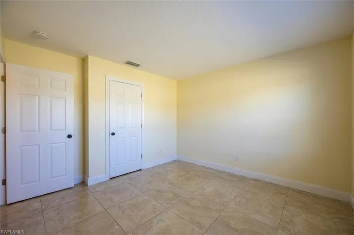 Room featuring light beige tiled flooring, pale yellow walls, white baseboards, and two paneled interior doors