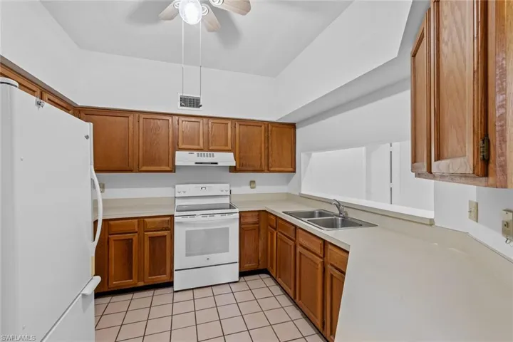 Kitchen with appliances, sink, ceiling fan, and light tile floors