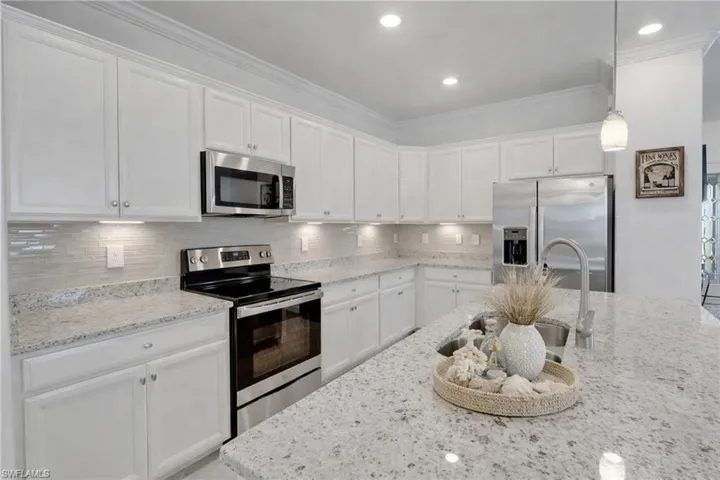 Kitchen with stainless steel appliances, white cabinetry, decorative backsplash, hanging light fixtures, and light stone counters