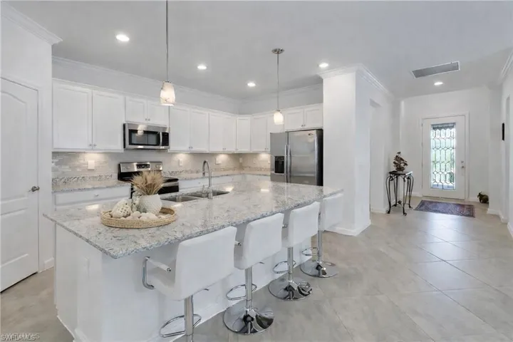 Kitchen featuring white cabinetry, stainless steel appliances, light stone countertops, decorative backsplash, and crown molding