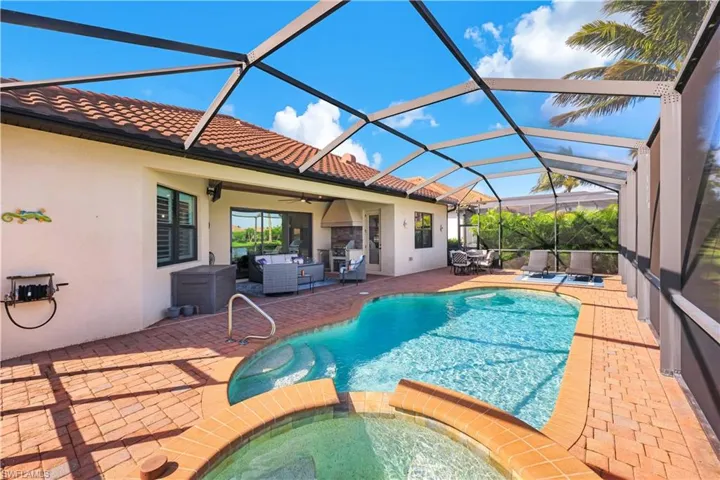 Screened-in lanai featuring a swimming pool, integrated spa, brick paver decking, and a built-in outdoor kitchen