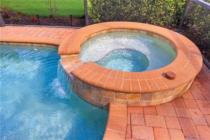 Raised circular spillover spa with tile surround, integrated water feature, and brick-paver decking enclosed within a screened lanai