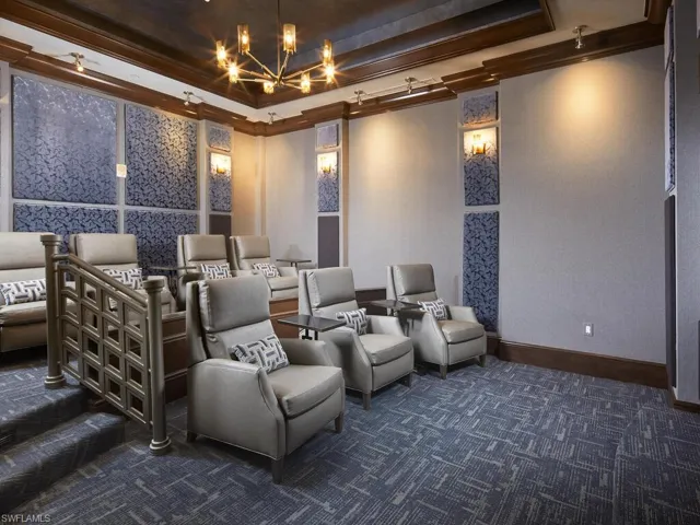 Cinema featuring an inviting chandelier, dark colored carpet, a raised ceiling, and crown molding