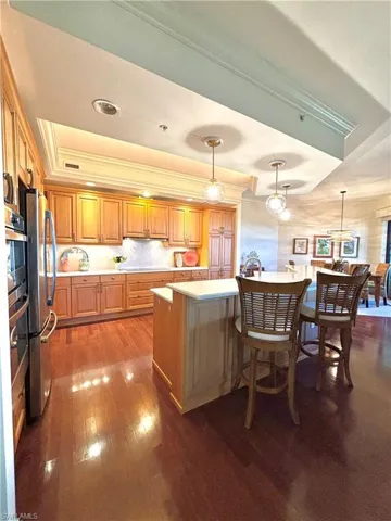 Kitchen featuring hanging light fixtures, dark hardwood / wood-style floors, stainless steel fridge, crown molding, and a breakfast bar