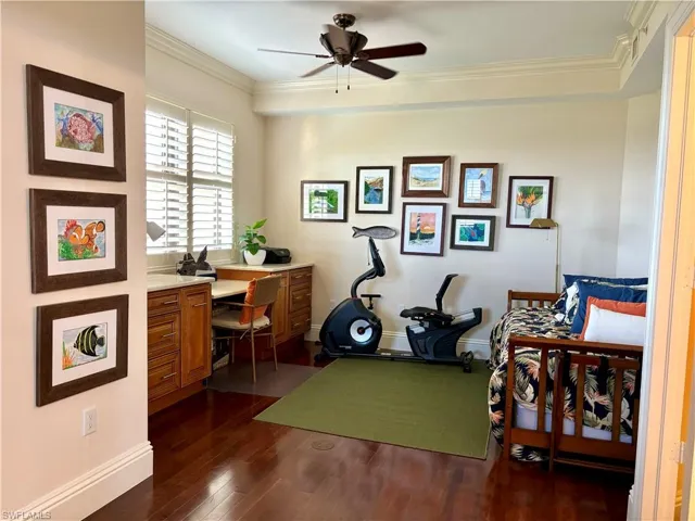 Office space featuring ceiling fan, ornamental molding, and dark wood-type flooring and built in cabinets and desk
